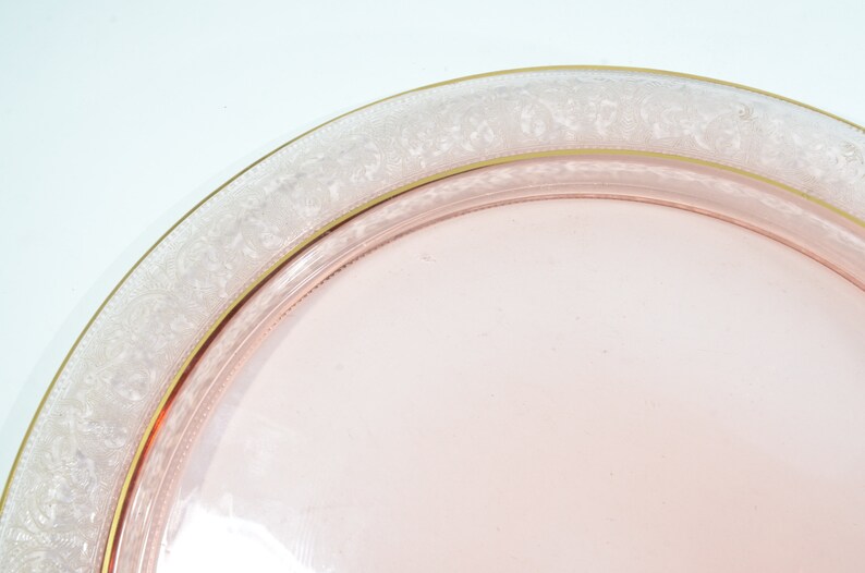 Puede incluir: Un plato de servir de vidrio rosa con un borde blanco y dorado. El plato tiene un delicado patr&oacute;n floral alrededor del borde.