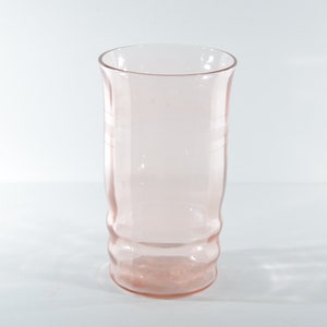 May include: A clear pink glass tumbler with a textured design. The glass is empty and has a rounded bottom.