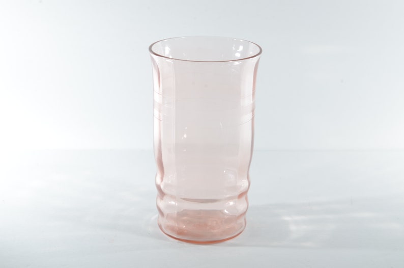 May include: A clear pink glass tumbler with a textured design. The glass is empty and has a rounded bottom.