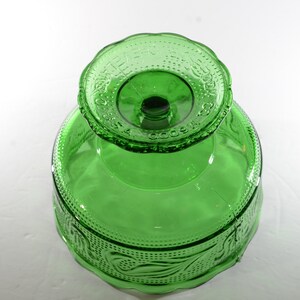 May include: A green glass pedestal bowl with a scalloped edge and a raised design of leaves and flowers. The bowl is made by the Anchor Hocking Glass Company.