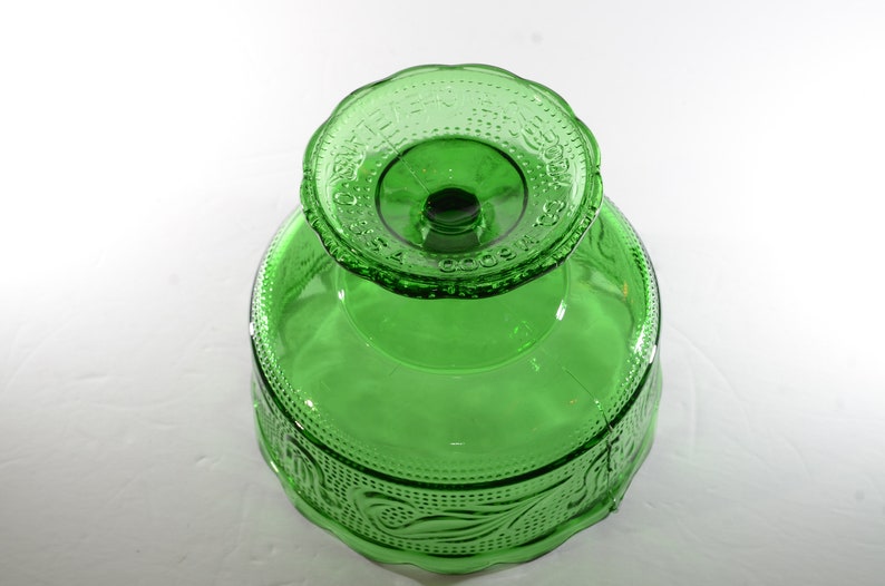 May include: A green glass pedestal bowl with a scalloped edge and a raised design of leaves and flowers. The bowl is made by the Anchor Hocking Glass Company.