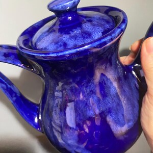 May include: A blue ceramic teapot with a white glaze. The teapot has a round body and a lid with a knob on top. The teapot is decorated with a swirling pattern of white and blue.