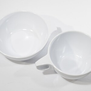 May include: Two white ceramic bowls, one with a handle and the other with a pouring spout. Both bowls are empty and appear to be made of a smooth, glossy material.