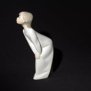 May include: A porcelain figurine of a girl in a white dress with blue trim, looking up and to the left.