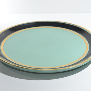 May include: A round, light green serving plate with a black and gold rim.