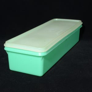 May include: A rectangular, mint green plastic container with a matching lid. The lid is a lighter shade of green. The container is likely for food storage. The container is on a black surface.