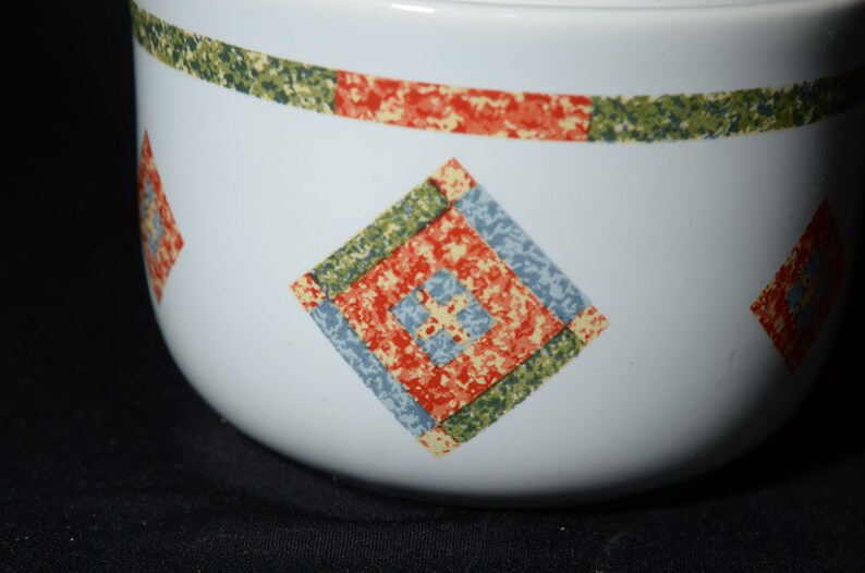 Puede incluir: Taz&oacute;n de cer&aacute;mica blanco con un patr&oacute;n geom&eacute;trico verde, rojo y azul. El patr&oacute;n es una serie de cuadrados dentro de cuadrados.