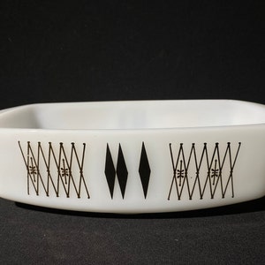 Puede incluir: Una fuente para horno Pyrex rectangular blanca con un patrón geométrico negro. El patrón incluye formas de diamante y líneas entrecruzadas. La fuente tiene esquinas redondeadas y una superficie lisa, ideal para hornear y servir.