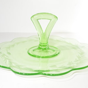 May include: A green glass serving tray with a scalloped edge and a handle. The tray has an etched design of leaves and berries.