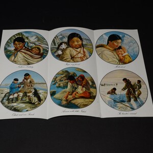 May include: A folded paper with six circular illustrations depicting Inuit life. Scenes include a mother with a baby, a girl with a puppy, and people fishing. The illustrations are set against a backdrop of mountains and water.