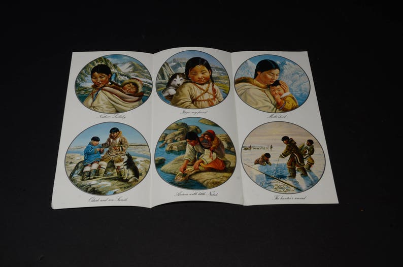 May include: A folded paper with six circular illustrations depicting Inuit life. Scenes include a mother with a baby, a girl with a puppy, and people fishing. The illustrations are set against a backdrop of mountains and water.