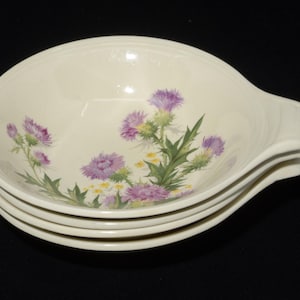 May include: A stack of four off-white ceramic bowls. Each bowl features a floral design with purple thistles, green leaves, and yellow flowers. The bowls have a handle-like extension on one side.