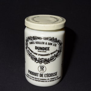 May include: A white ceramic jar with a black label that reads "JAMES KEILLER & SON LTD. DUNDEE MARMELADE D'ORANGES SEVILLE PRODUIT DE L'ÉCOSSE 12 OZ. LTD."