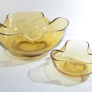 May include: A set of two amber glass bowls with a wavy, organic shape. The larger bowl is wider and shallower than the smaller bowl.