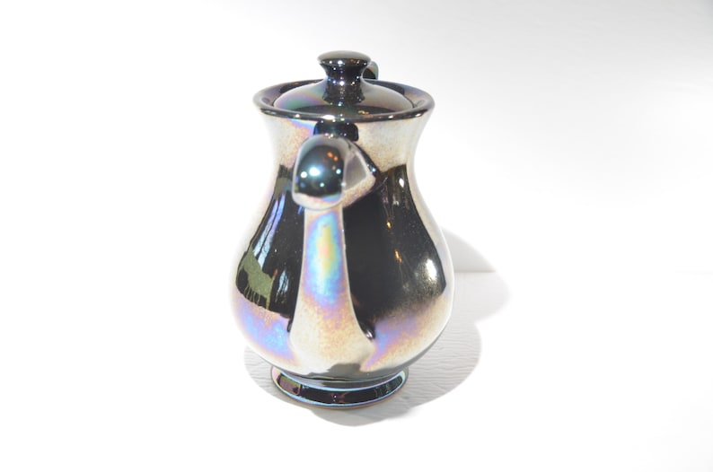May include: A silver iridescent ceramic creamer with a lid and a handle. The creamer has a pearlescent finish.