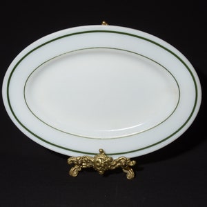May include: White oval serving platter with a green rim. The platter is on a gold metal stand.