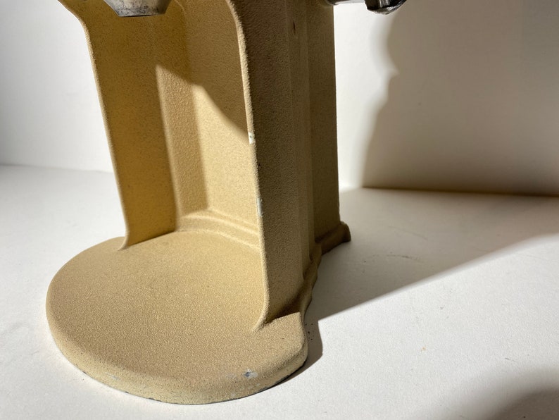 May include: Close-up of the base of a beige electric coffee grinder. The base is made of a textured material and has a rounded shape.
