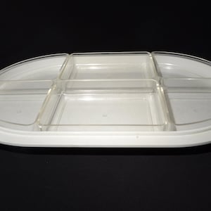 Może przedstawiać: Biała owalna taca do serwowania z przezroczystymi plastikowymi przegródkami. Taca ma podniesioną krawędź i jest podzielona na kilka sekcji do serwowania przekąsek lub przystawek. Przezroczyste przegródki są prostokątne i owalne.
