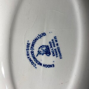 Op de afbeelding: Een close-up van een wit keramiek bord met een blauw en wit logo. Het logo luidt "Enoch Wedgwood (Tunstall) Ltd." en "Engeland Handelsmerk Gevestigd in 1835".