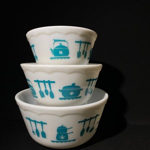 May include: A set of three white mixing bowls with a blue and white kitchen utensil design. The bowls are stacked on top of each other.