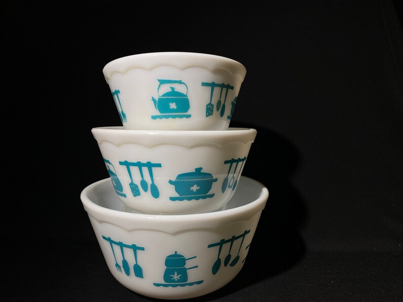 May include: A set of three white mixing bowls with a blue and white kitchen utensil design. The bowls are stacked on top of each other.