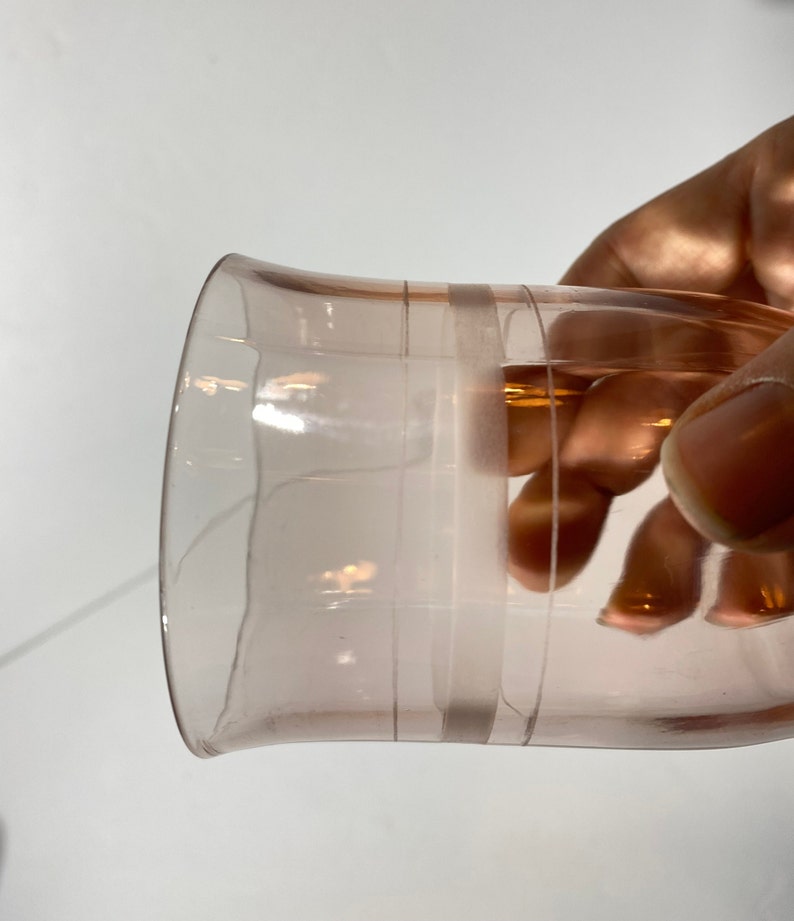 May include: A clear pink glass with a wide rim and a slightly flared base. The glass has two horizontal lines around the middle.