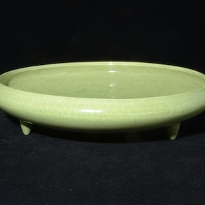 May include: A pale green, oval ceramic bowl with three small feet. The bowl has a speckled texture and a glossy finish. The design is simple and elegant, suitable for various decorative or functional uses.