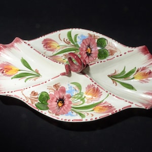 May include: A white ceramic serving dish with three sections, featuring a hand-painted floral design in shades of pink, red, yellow, and green. The dish has a unique twisted handle.