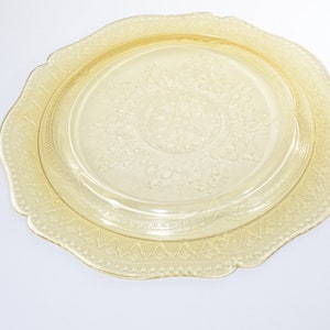 May include: A yellow glass plate with a scalloped edge and a raised floral design. The plate is perfect for serving desserts or appetizers.