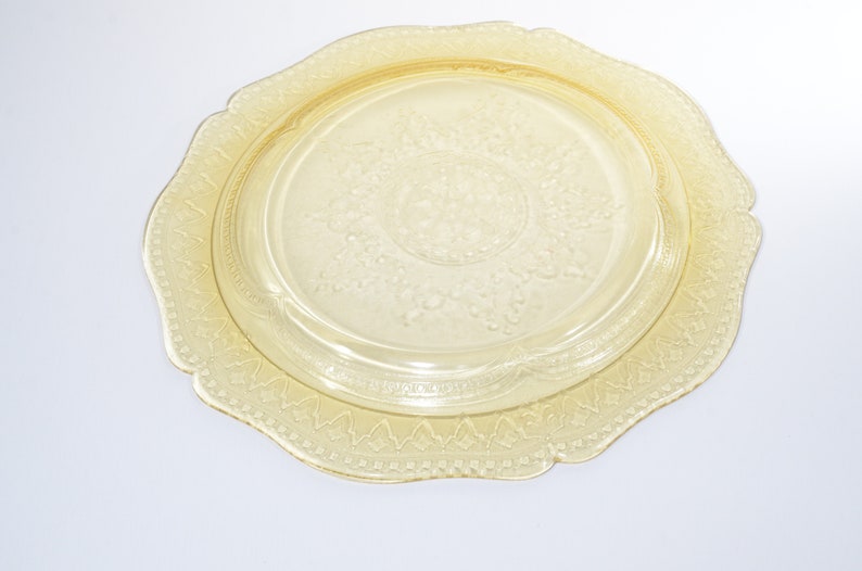 May include: A yellow glass plate with a scalloped edge and a raised floral design. The plate is perfect for serving desserts or appetizers.