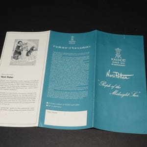 May include: A tri-fold brochure for Kaiser Porcelain, featuring artist Nori Peter. The teal cover displays the text "Nori Peter" and "People of the Midnight Sun". The brochure has white interior pages with text and an illustration.