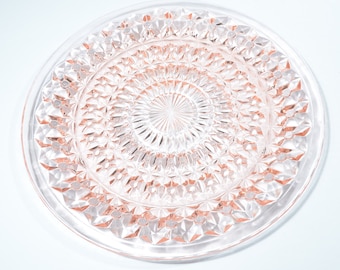 Pode incluir: Um prato de vidro rosa claro com um padrão de diamante. O prato é redondo e tem um centro elevado.