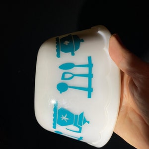 May include: White ceramic bowl with a blue and white kitchen themed design. The design features a teapot, a pot, and utensils.