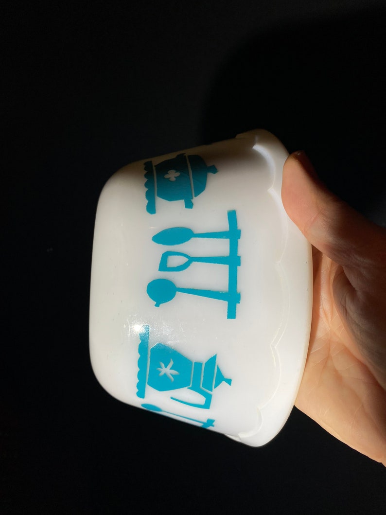 May include: White ceramic bowl with a blue and white kitchen themed design. The design features a teapot, a pot, and utensils.