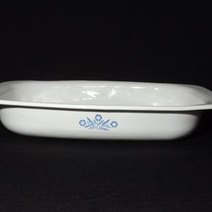 Puede incluir: Plato rectangular para hornear blanco con un diseño floral azul. El plato está hecho de cerámica y tiene un acabado liso y brillante.