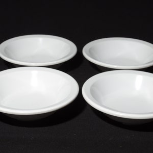 May include: Four white ceramic bowls, all the same size and shape, are arranged in a square pattern on a black surface.
