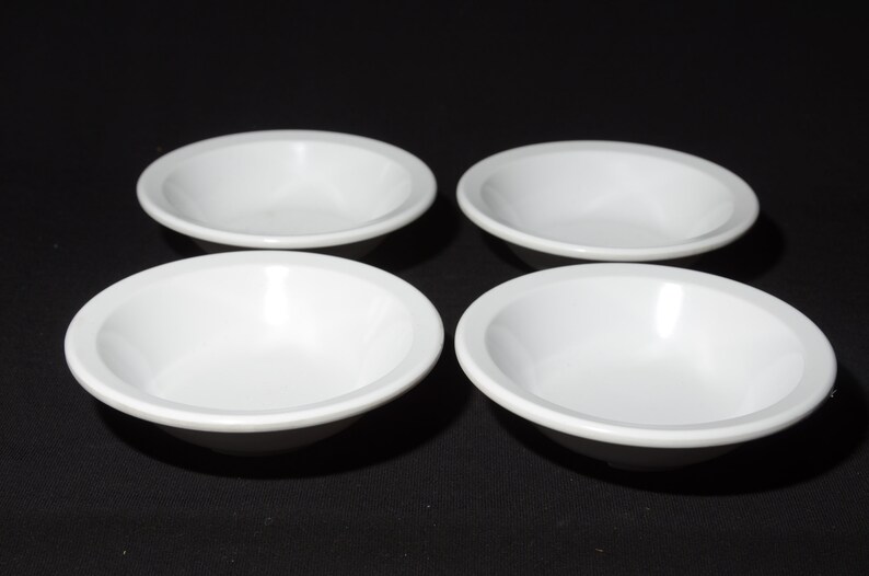 May include: Four white ceramic bowls, all the same size and shape, are arranged in a square pattern on a black surface.