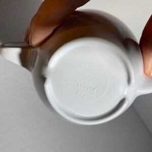 May include: White ceramic teapot with a handle and spout. The bottom of the teapot has the text "C.P. Melmac 1 qt. Made in Japan" printed on it.