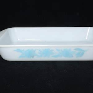 Puede incluir: Fuente rectangular blanca para horno con esquinas redondeadas. Presenta un estampado floral azul claro en el lateral. Un clásico para hornear y servir, de unos 25 cm de largo.