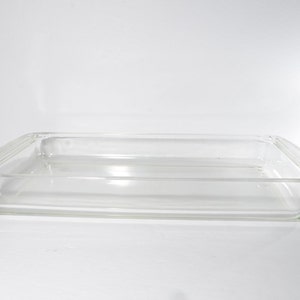 Puede incluir: Un molde para hornear rectangular de vidrio transparente con bordes ligeramente elevados.