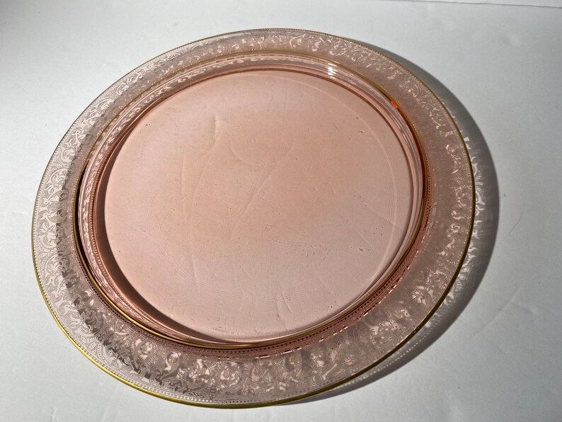 Puede incluir: Un plato de servir de vidrio rosa con un borde dorado y un delicado dise&ntilde;o grabado alrededor del borde.