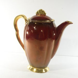 May include: A red and gold ceramic coffee pot with a fluted body and a gold handle.