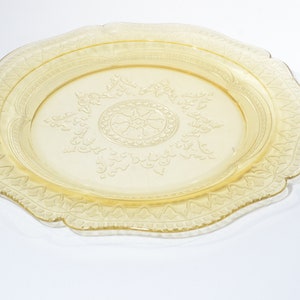 May include: A yellow glass plate with a decorative, embossed design. The plate has a scalloped edge and a raised center design.