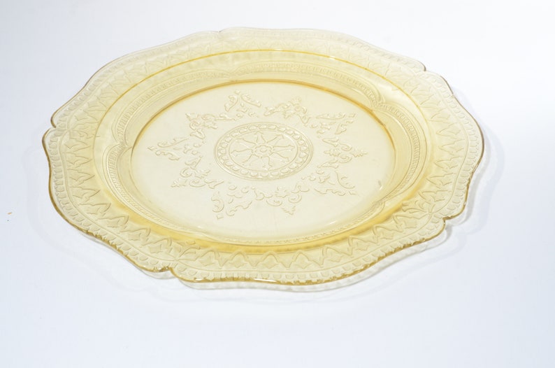 May include: A yellow glass plate with a decorative, embossed design. The plate has a scalloped edge and a raised center design.