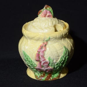 Peut inclure: Un pot à miel en céramique jaune avec un couvercle décoré de fleurs roses et vertes. Le pot a un motif floral et un petit trou dans le couvercle pour verser.