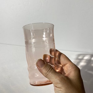 May include: A pink glass drinking glass with a slightly flared rim and a textured design. The glass has a band of clear glass around the middle.