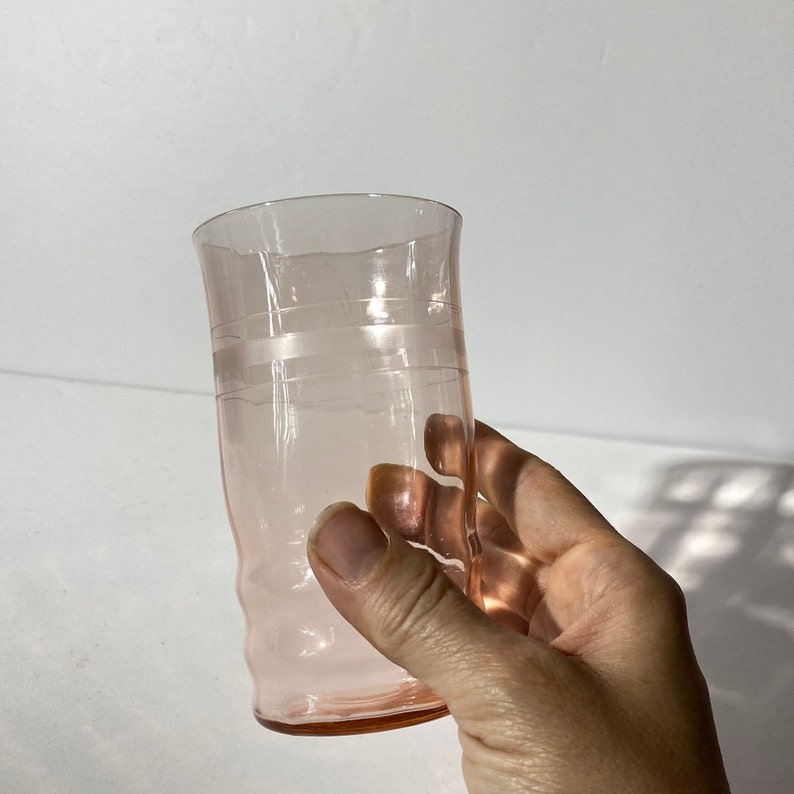 May include: A pink glass drinking glass with a slightly flared rim and a textured design. The glass has a band of clear glass around the middle.