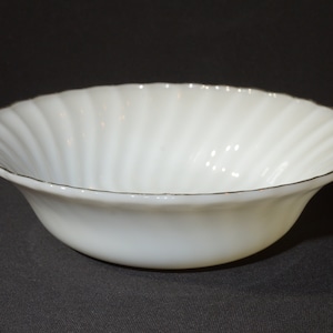 Puede incluir: Tazón blanco de vidrio lechoso con un borde dorado. El tazón tiene un diseño acanalado.