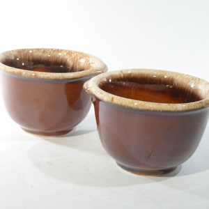 May include: Two brown ceramic bowls with a white glaze around the rim. The bowls are slightly different sizes and have a mottled brown glaze.