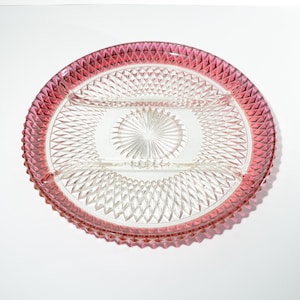 Può includere: Un piatto da portata in vetro trasparente con un bordo rosa e un motivo a diamante. Il piatto è diviso in tre sezioni.